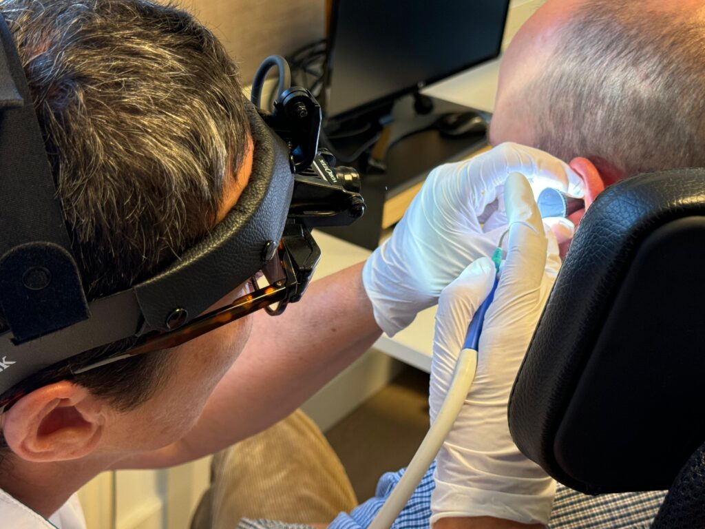 Doktersassistent Monique Danenberg verwijdert oorsmeer met hoofdgedragen microscoop en vacuumpomp